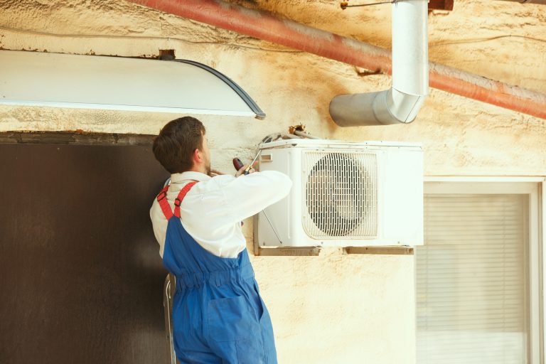 HVAC technician working on a capacitor part for condensing unit. Male worker or repairman in uniform repairing and adjusting conditioning system, diagnosting and looking for technical issues.